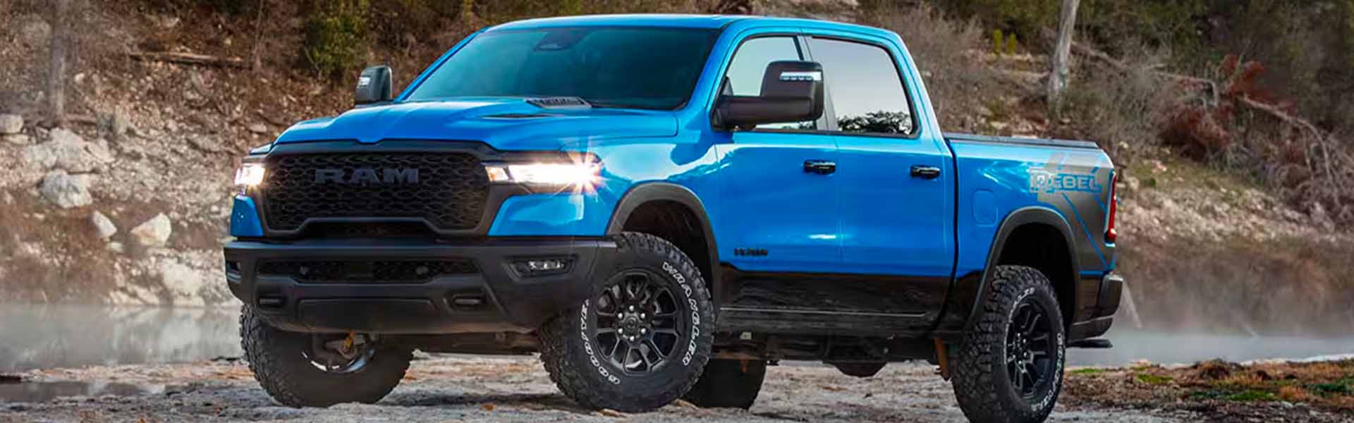 A blue RAM 1500 Rebel pickup truck parked on a rocky shoreline.