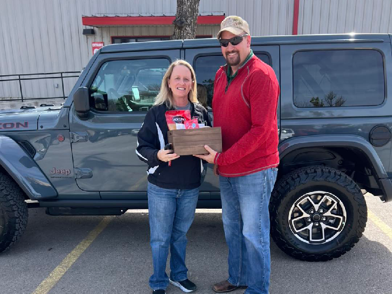 Adults stand smiling outdoors in front of a school building.