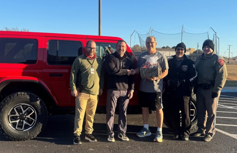 Adults stand smiling outdoors in front of a school building.