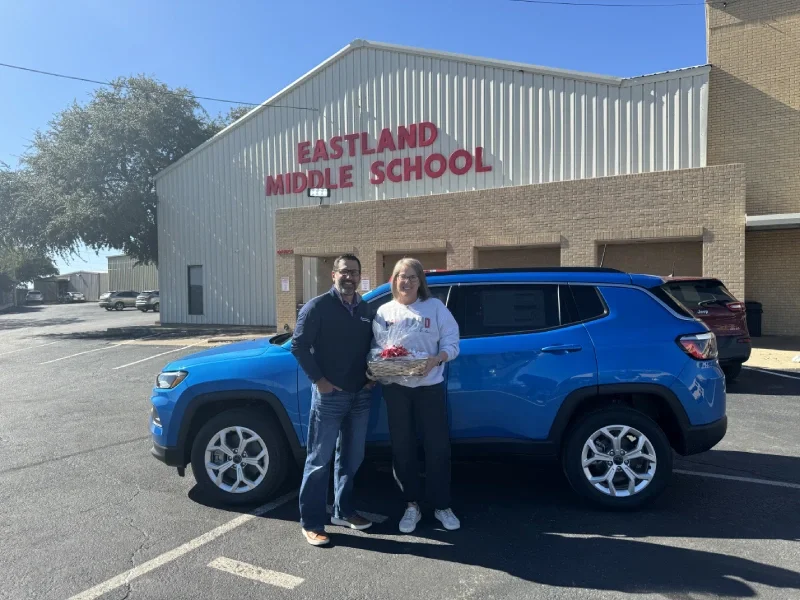 A couple of adults pose next to a blue vehicle outside the school.