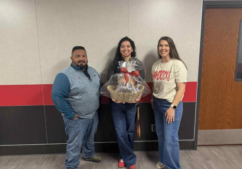 Adults stand smiling outdoors in front of a school building.