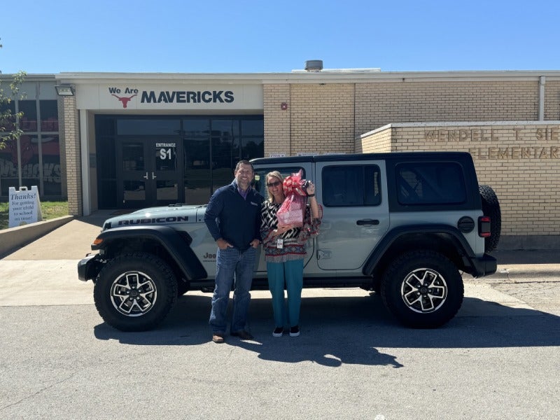 A woman poses alone next to a white SUV outside the school.