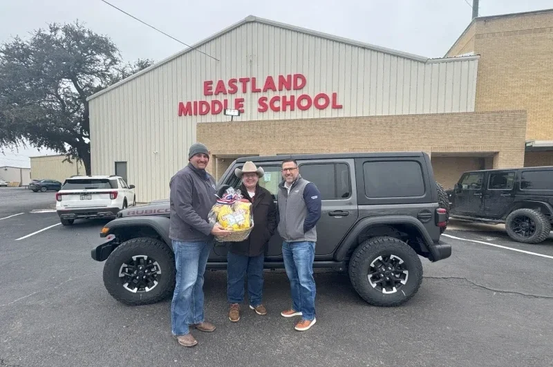 A couple of men giving gift to a woman standing next to SUV.