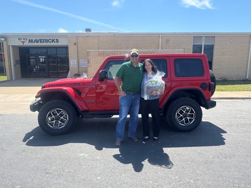 Adults stand smiling outdoors in front of a school building.