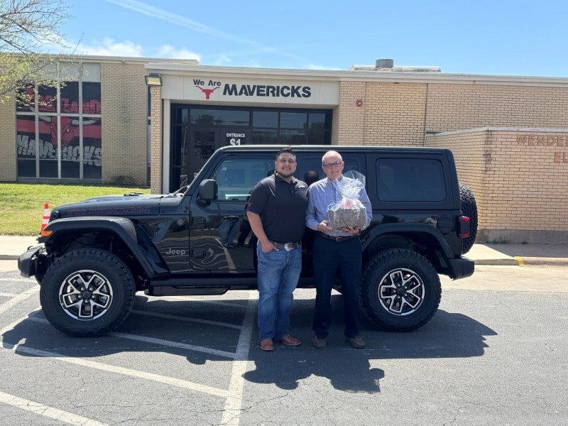 Adults stand smiling outdoors in front of a school building.
